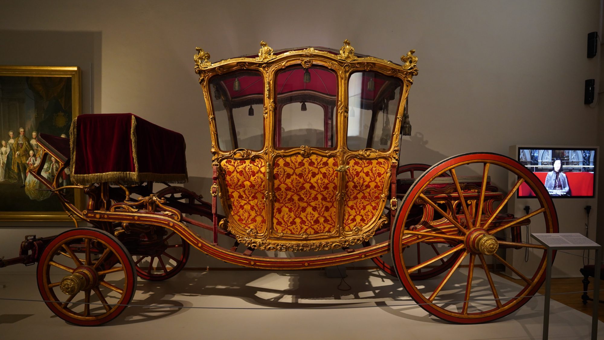 A small and beautiful carriage decorated in gold and bronze with red and gold leaf patterns on the doors