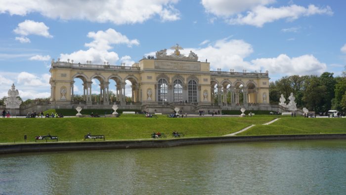 The Gloriette, a large colonnated arcade overlooking a pond, under a mostly blue sky