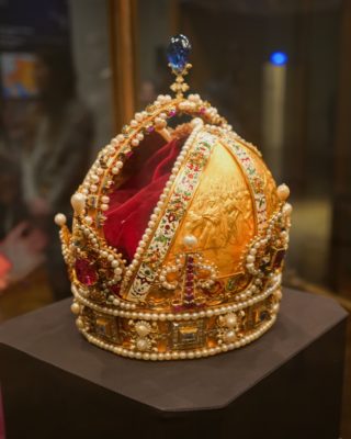 A gold domed crown covered in pearls and gems, with red lining