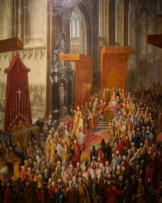 A painting of the coronation of Joseph II. There is a big crowd, and Joseph II is dubbed with a sword