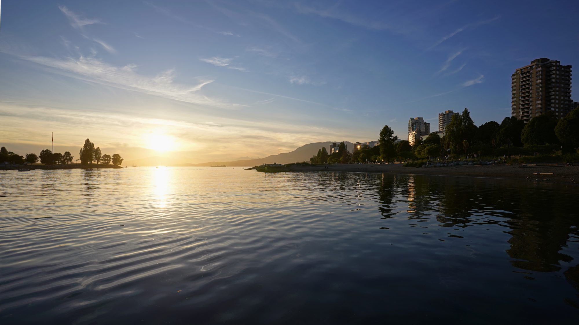 A sunset seen over the water. The sky is mostly clear, and the very low sun is reflected on the still water