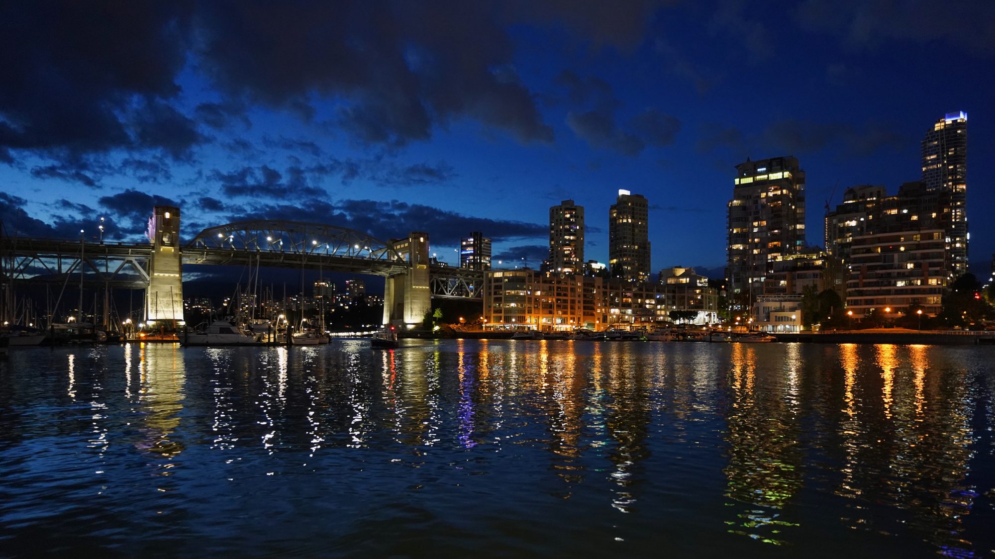 Burrard Bridge and some downtown towers, at twilight. The sky is a deep blue and city lights are reflected in the water