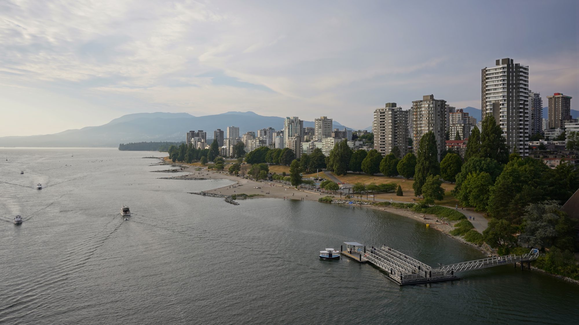 A view of the West End towers and Sunset Beach from Burrard Bridge. There are wispy clouds in the sky, and the light is fading