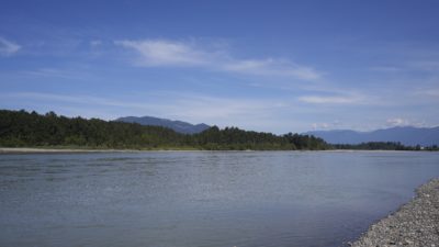 The Fraser River, with a gravelly beach in the foreground and some tree-covered hills on the other side