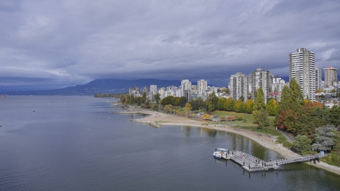 A view of West End towers from Burrard Bridge. The towers and beach are brightly lit, while the sky is darker and overcast